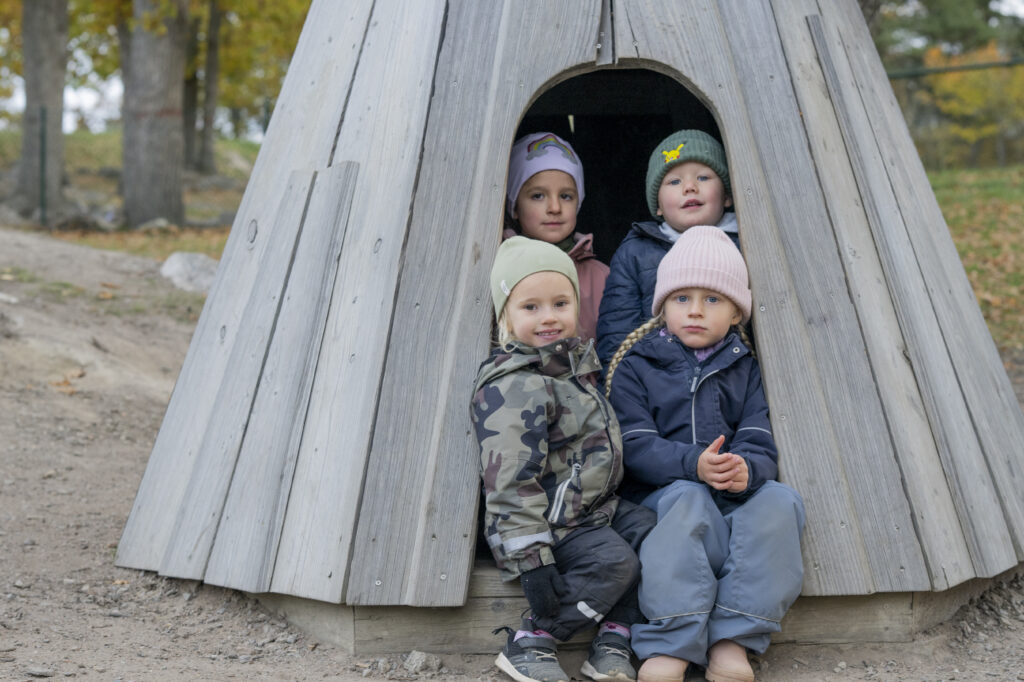 Förskolebarn som sitter tillsammans i en träkoja utomhus