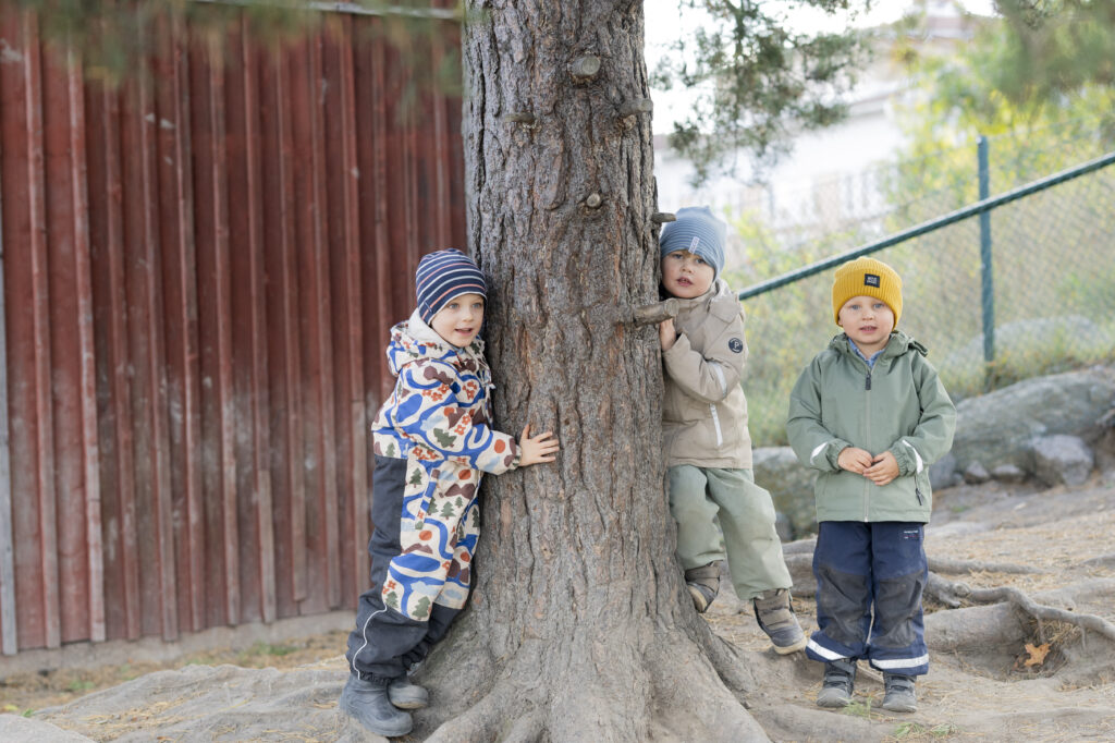 Förskolebarn som står runt en tall